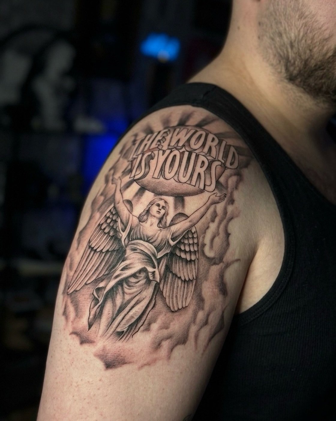 Omuz melek ve The World Is Yours yazısı dövmesi — bulutlu black & grey | Titan Ink Gallery Samsun